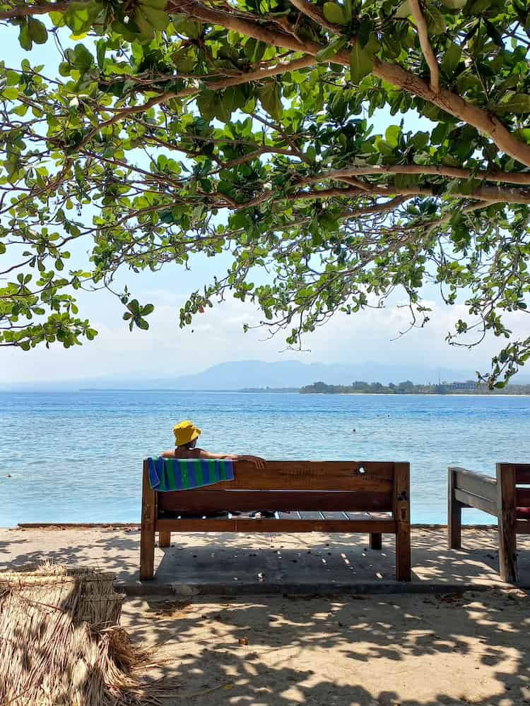 Una donna in super relax guarda il mare seduta su una panchina