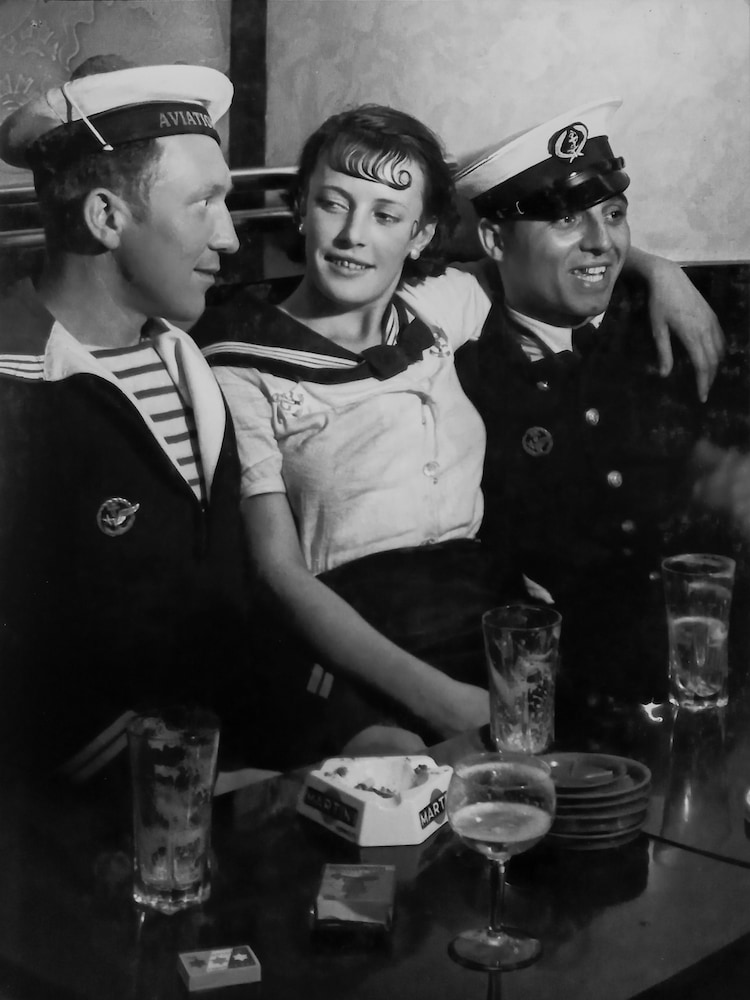 brassai in mostra a milano: una ragazza in mezzo a due marinai in un bistrot