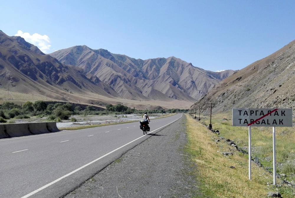 Podcast di viaggio: un ciclista su una strada in mezzo a una vallata del Kirghizistan