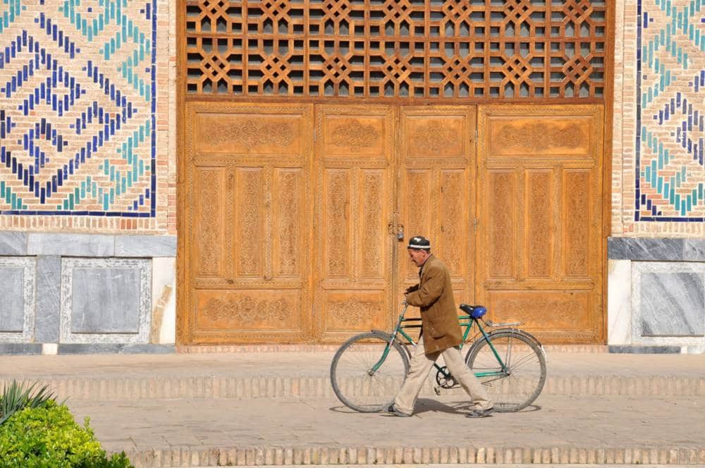 Podcast di viaggio: un uomo in bicicletta davanti a un antico palazzo in Uzbekistan
