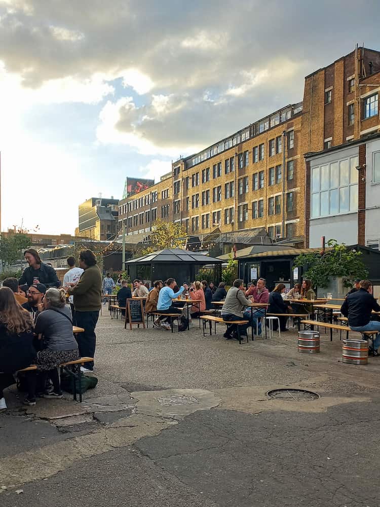 tavolini e persone sedute nel cortile di copeland park nel quartiere di Peckham